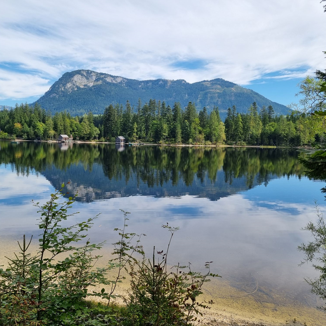 Ein Berg spiegelt sich im See, Wolken ziehen über den Berg.